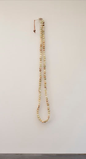 Tasbih, a long hanging strand of pale green onyx beads photographed against a wall